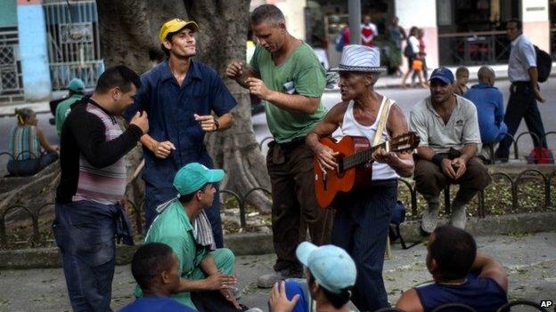 Construction workers dance and sing with a street musician while they wait for the bus to return home at the end of the workday repairing the streets of the old town in Havana (15 October 2014)