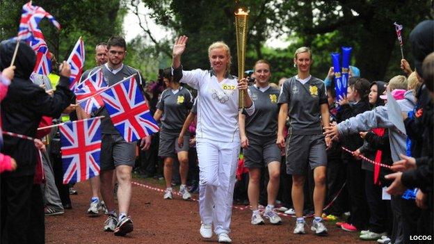 Spectators wave Union Jack flags as Torchbearer 037 Laura Graves carries the Olympic Flame through Sherwood Forest whilst holding the Olympic Flame on Day 41 of the Olympic Flame Torch Relay leg on June 28, 2012 in Nottingham, England. The Olympic Flame is now on day 41 of a 70-day relay involving 8,000 torchbearers covering 8,000 miles. (Photo by LOCOG via Getty Images)