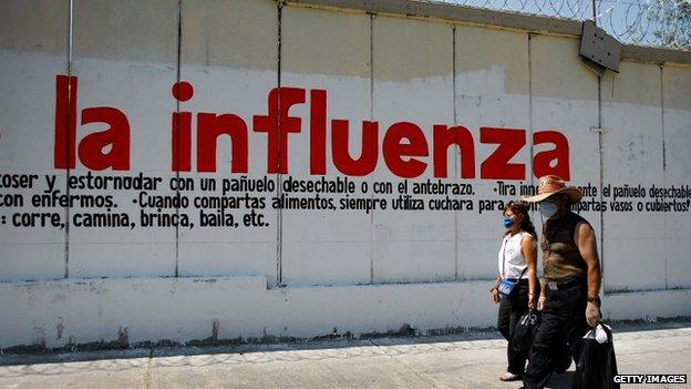 People walk past sign warning of influenza on 1 May 2009 in Mexico City