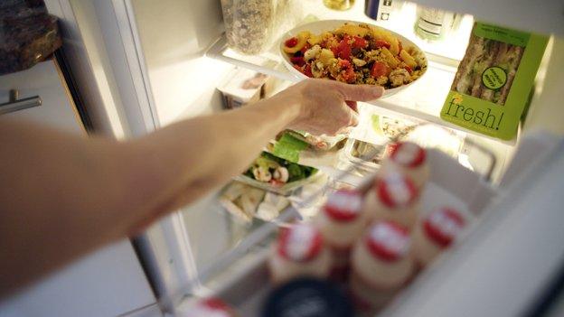 Arm of person putting pasta dish in fridge