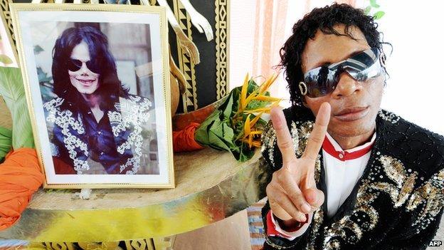 A Michael Jackson fan poses for a portrait next to the framed picture of his idol on 4 July 2009 in Abidjan's palace of culture during a homage ceremony held for the deceased artist
