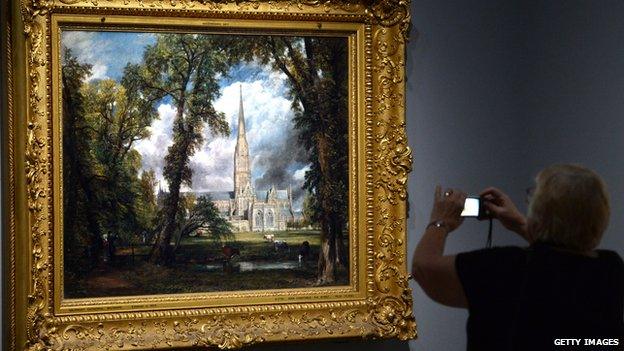 A woman photographs a painting by British artist John Constable entitled 'Salisbury Cathedral from the Bishops Grounds'