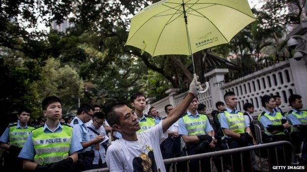 A pro-democracy protester holds an umbrella in front of police guarding Government House after a march from the Admiralty protest site in Hong Kong, 22 October 2014