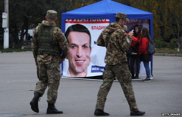 Ukrainian soldiers patrol near a tent with an electoral poster in Sloviansk (22 Oct)