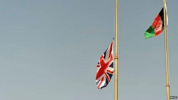 A UK flag being lowered as an Afghan flag flies