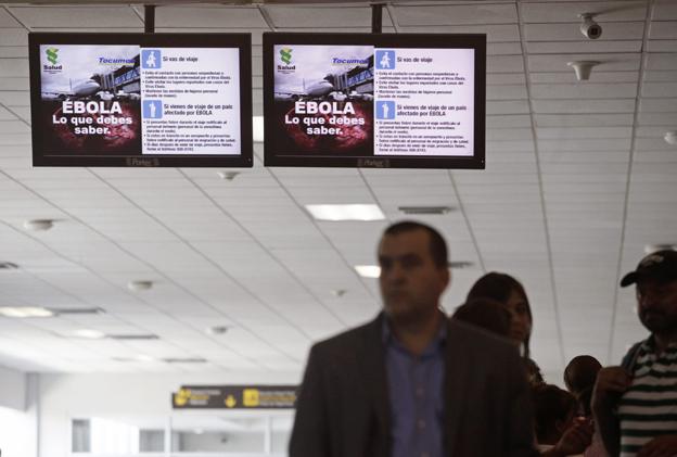 Passengers stand underneath screens explaining Ebola symptoms at Tocumen International Airport in Panama City