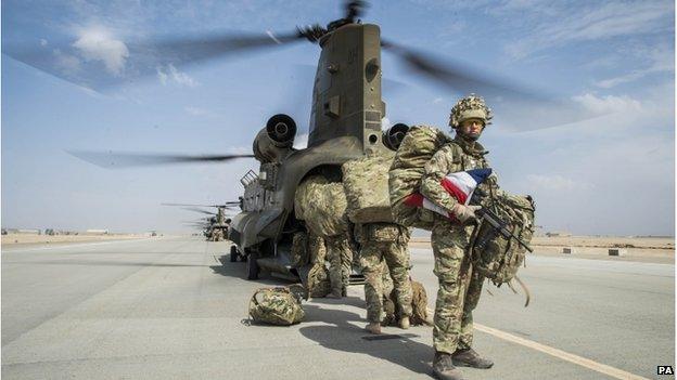 A British serviceman in full kit holding a UK flag