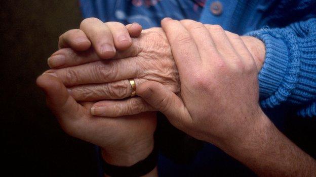 Carer holds the hand of an elderly patient