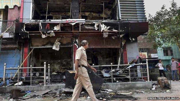 A policeman walks past a burnt shop in Trilokpuri, New Delhi