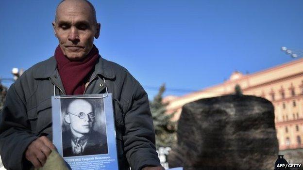 A man holds his father's portrait near the memorial to the victims of Soviet-era political repression, the Solovky Stone monument, on Lubyanka Square in Moscow, on October 29, 2014