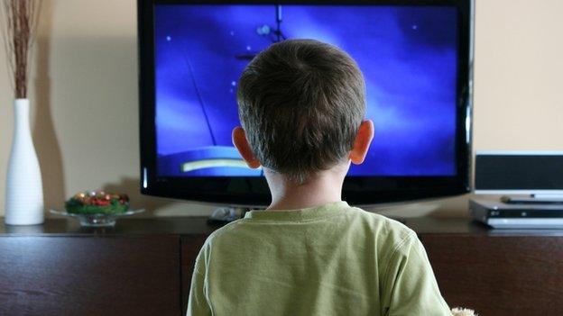 A boy stands in front of a television screen.