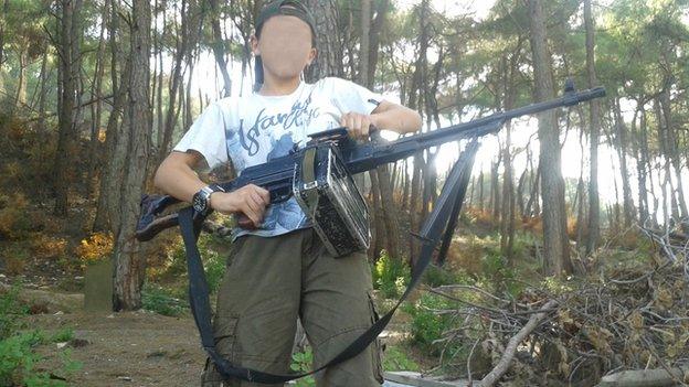 A 13-year-old boy who wishes to be named 'Abu Hattab' stands in a forest holding a weapon