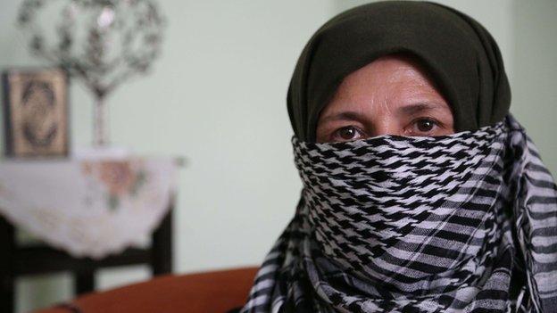 The mother of a 13 year old IS fighter sit in her house wearing a chequered scarf across her face