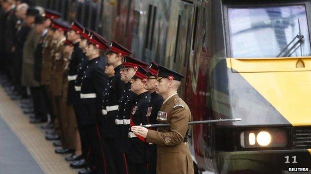 Military personnel and veterans line the platform as a train with commemorative wrap for the fallen of World War One pulls into the station at King's Cross