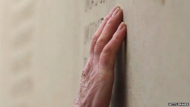 A woman's hand traces a name on a memorial