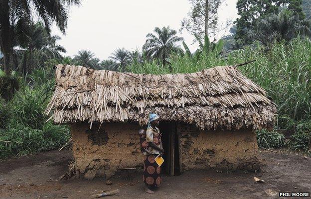 A mother with her child stands holding a vaccination card outside her home in the village of Kishee