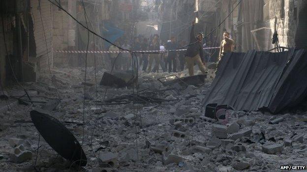 Syrians stand in a street filled with debris following a reported barrel bomb attack by government forces in the northern Syrian city of Aleppo on 31 October 2014