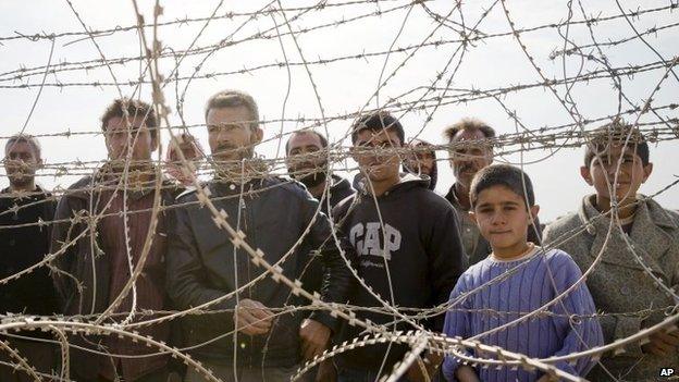 Syrian Kurds stand behind a barbed wire fence that marks the Turkey-Syria border on the outskirts of Kobane, 14 November 2014