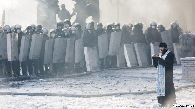 An Orthodox priest prays between police and protesters at the scene of anti-government protests in Kiev (January 2014)