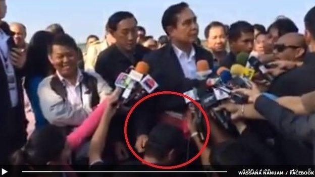 Thai prime minister surrounded by journalists, patting one on the head