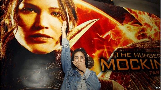 Thai pro-democracy activist Nacha Kong-udom closes her mouth and flashes a three-finger salute in front of a poster of The Hunger Games movie at a cinema in Bangkok, Thailand, 20 November 2014