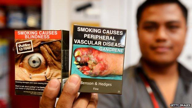 A shopkeeper with two packets of plain packaged cigarettes