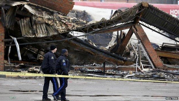 Police officers look over the site of a building that was burned in riots the previous night in Ferguson, Missouri 25 November 2014