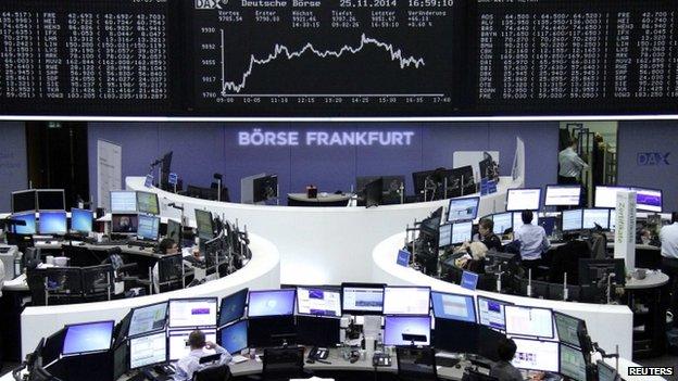 Traders at their desks in front of the German share price index DAX board at the Frankfurt stock exchange (25 November 2014)