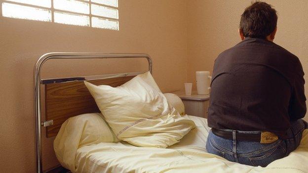 A man sits on his bed in a mental health ward