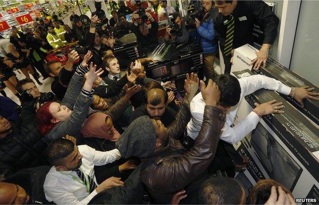 People in a shop pushing to get to televisions