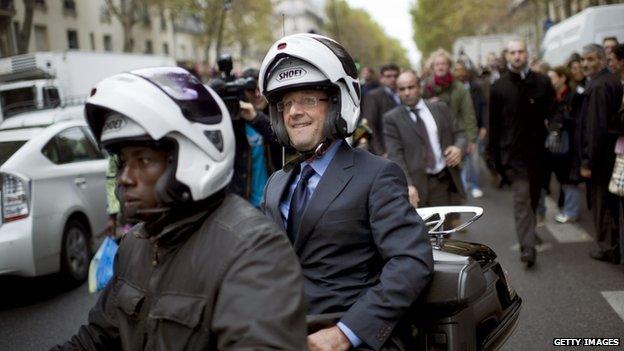 Francois Hollande rides on the back of a scooter while campaigning in Paris, 11 October 2011