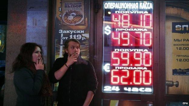 Russians smoke next to electronic boards showing exchange rates