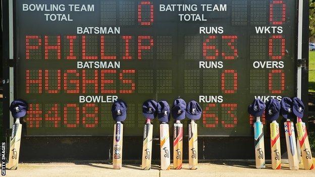 Cricket bats and caps belonging to the players are placed near the scoreboard which displays a tribute to Phillip Hughes