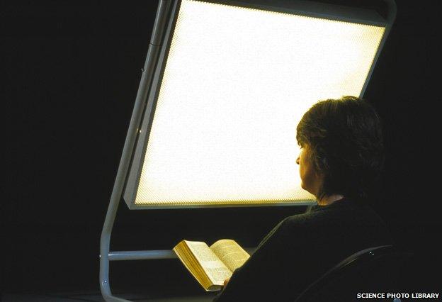 Woman reading a book as she undergoes phototherapy in front of a light screen