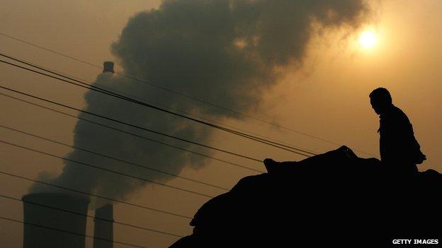 A Chinese man squats on a truck near a power plant emitting plumes of smoke from industrial chimneys on 30 October 2007 in Beijing, China.