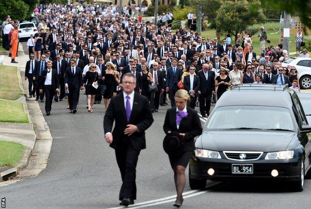 A large procession of mourners walk through the streets of Macksville