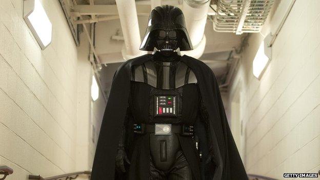 A man in a Darth Vader costume walks down a hallway.