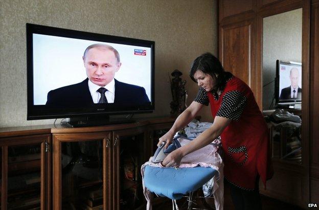 A woman irons clothes as Vladimir Putin speaks on a TV screen in Moscow, 4 December