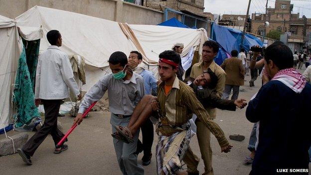 Young men holding up an injured friend run through Sanaa on 13 March 2011