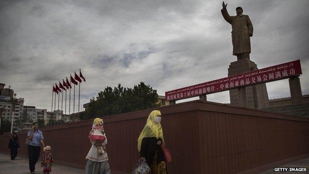 Uighur women walk past a statue of Mao in Kashgar