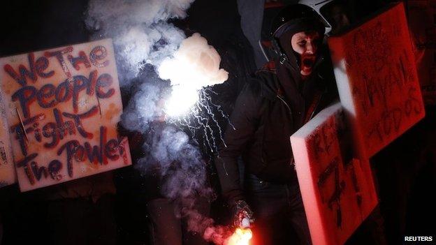 A demonstrator holds a flare during a protest in front of La Scala opera house on the first day of opera season in downtown Milan (7 December 2014)