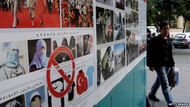 Pedestrians walk past anti-terror propaganda posters pasted along the streets of Urumqi, far west China's Xinjiang region on 16 September, 2014