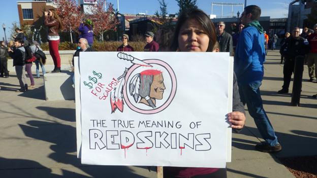 A person at a protest in Minnesota holding up a sign criticising the use of the world "redskin"