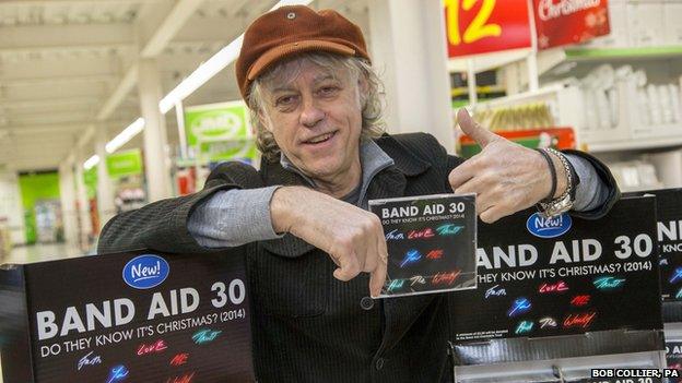 Bob Geldof holds a Band Aid CD single and gives a thumbs up to the camera