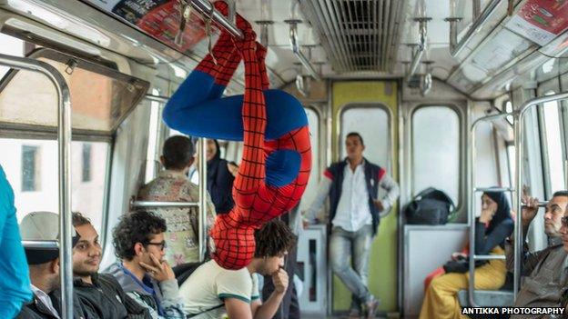 A man dressed as Spider-Man hangs upside down from a rail on the Cairo metro