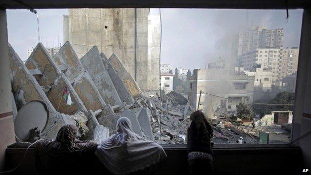 A Palestinian family looks through a window at the remains of the 13-storey al-Basha Tower in Gaza City (26 August 2014)