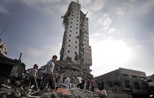 Palestinians walk past the Italian Complex after an Israeli air strike in Gaza City (26 August 2014)