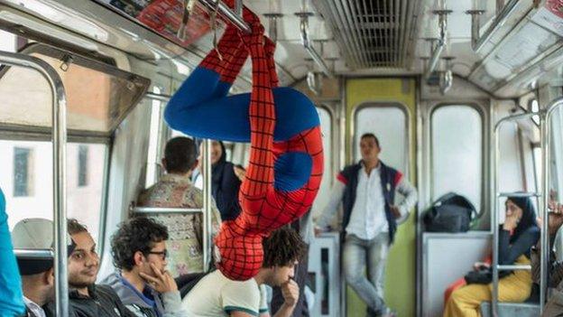 A man dressed as Spider-Man hangs upside down from a rail on the Cairo metro
