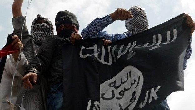 Kashmiri demonstrators hold up a flag of the Islamic State