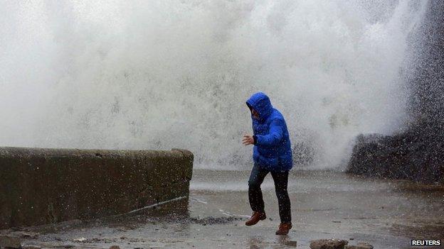 A man runs as a huge wave breaks on a sea wall nearby